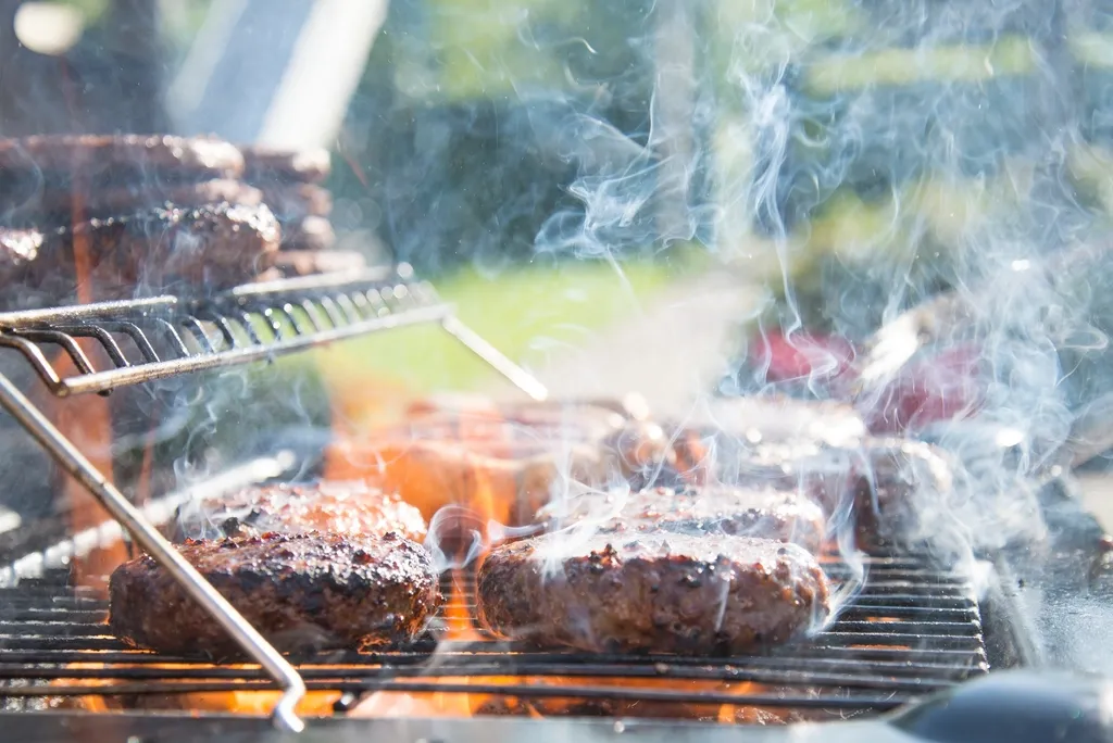 Burgers and meat searing on a backyard grill with smoke rising