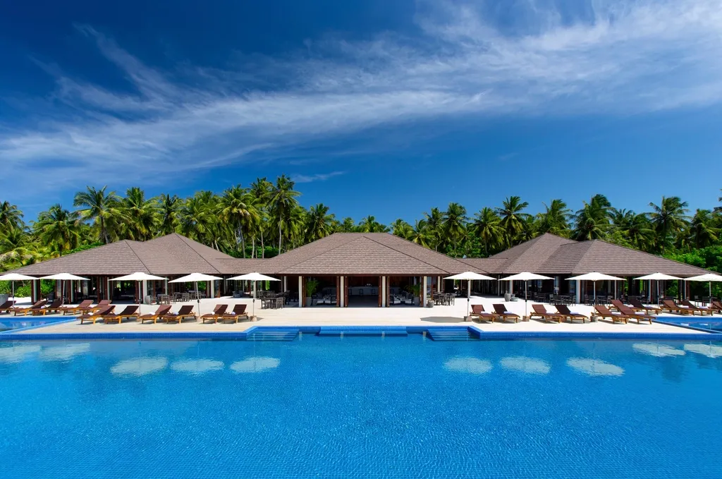 A wide resort-style pool with villa pavilions, white umbrellas and loungers backed by a wall of palm trees