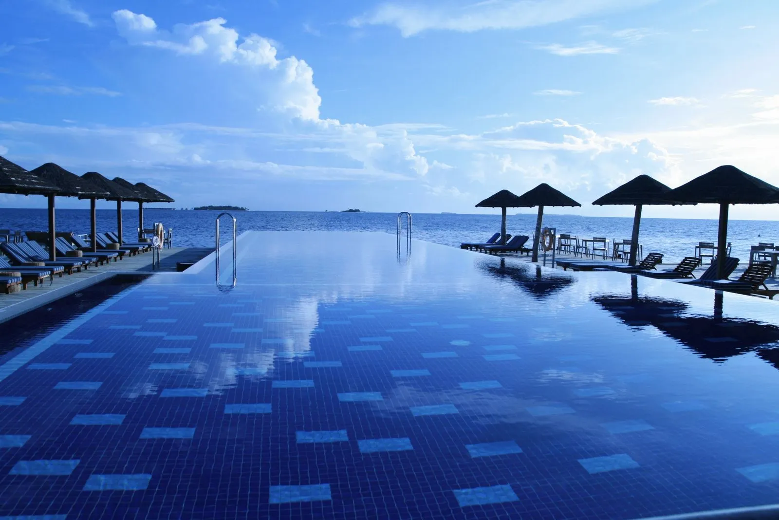 Upright resin chairs lined along the shallow shelf of a bright blue swimming pool