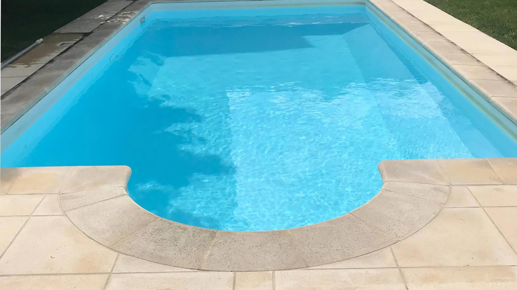 A backyard swimming pool with clear blue water, a stone coping edge and a rounded step corner
