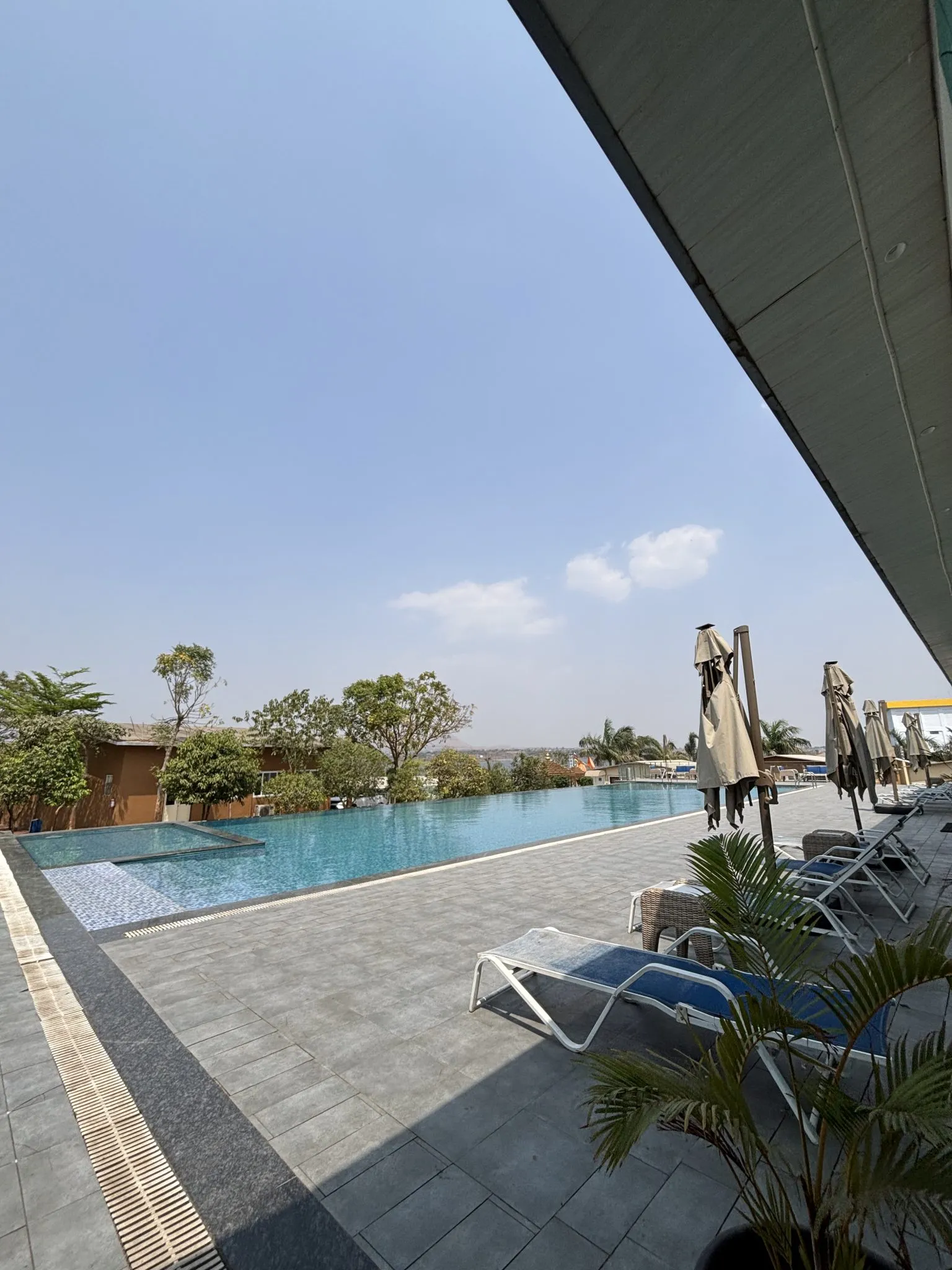 Poolside umbrellas and lounge chairs beside an infinity pool under a clear blue sky