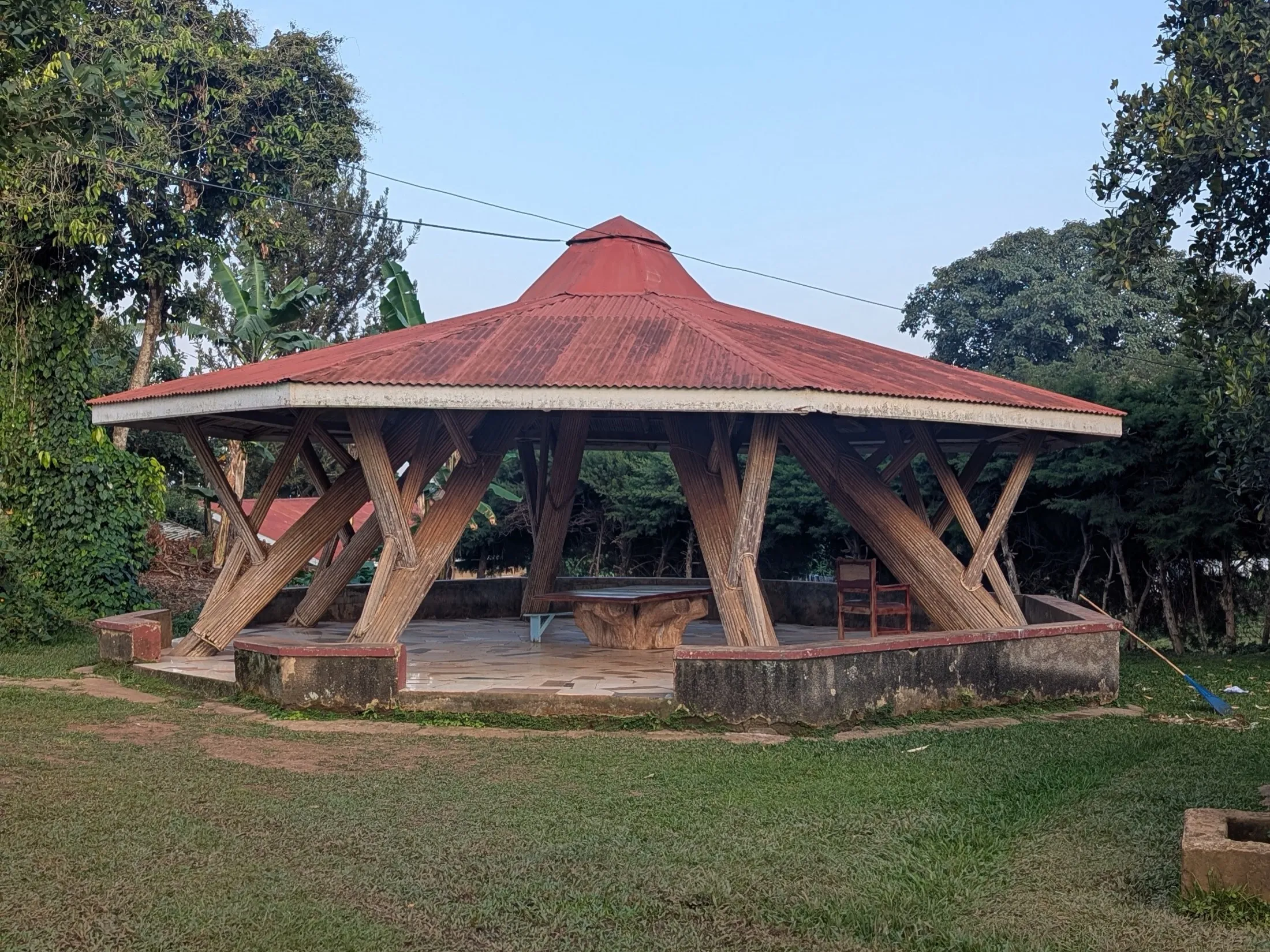 A wood-post gazebo with a corrugated metal roof standing on a lawn