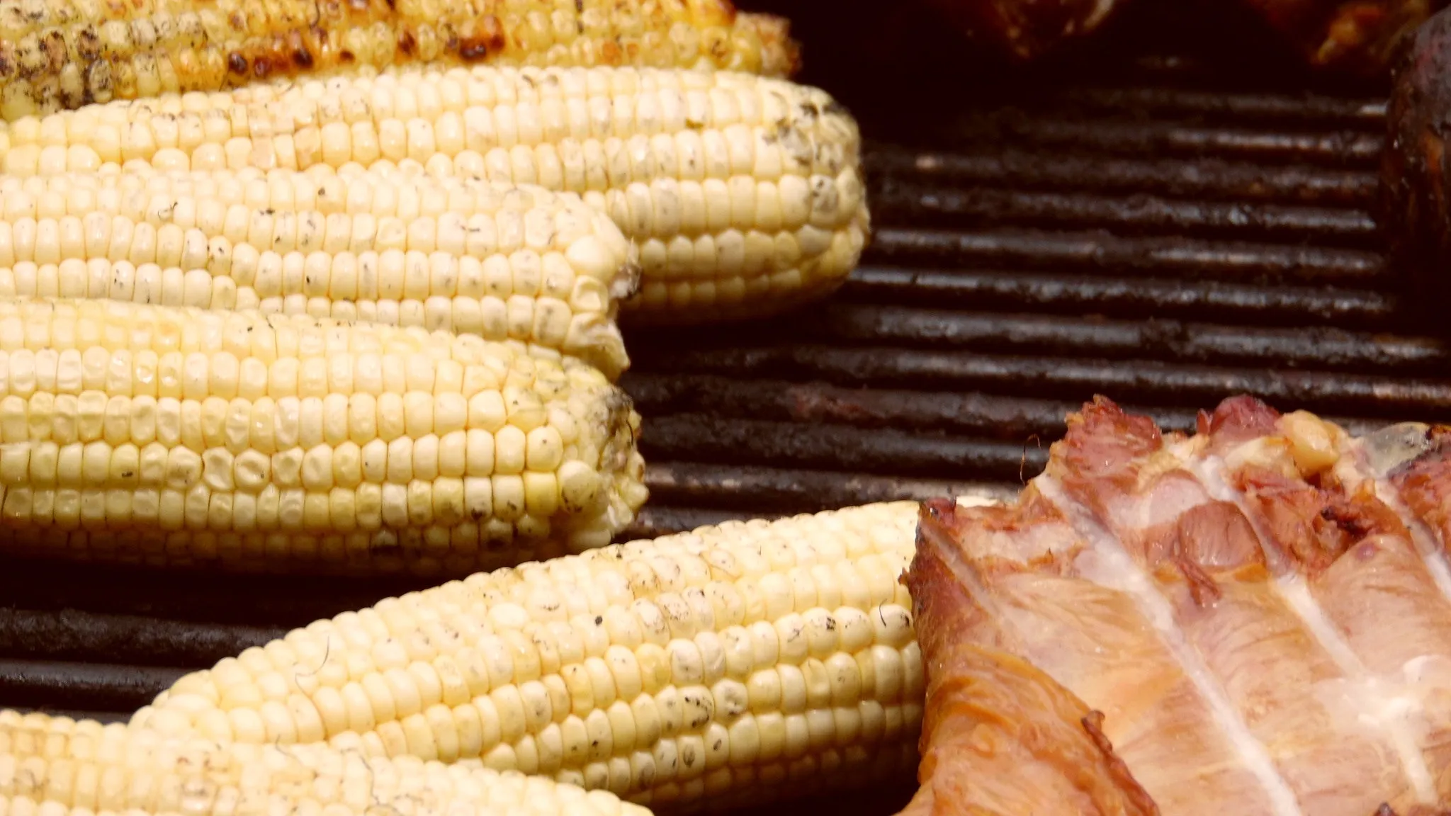 Ears of grilled corn and a rack of meat side by side on a grill grate