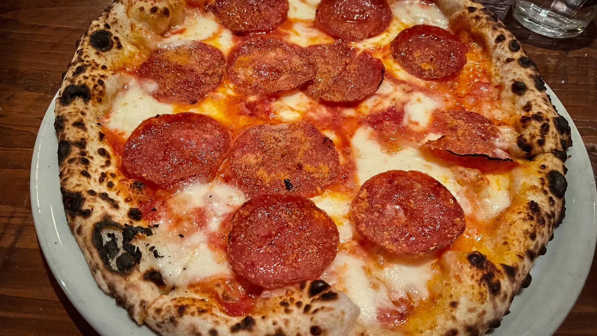 A Neapolitan-style pepperoni pizza on a white plate, its crust spotted black from a very hot oven