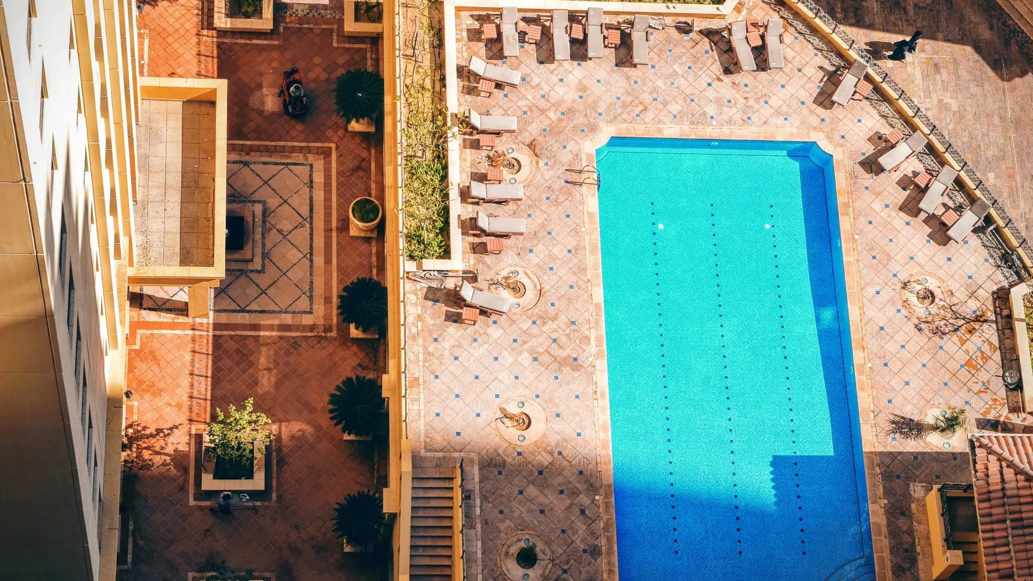 Looking down on a pool deck lined with white loungers and small side tables between them, the spot a deck box side table is bought for