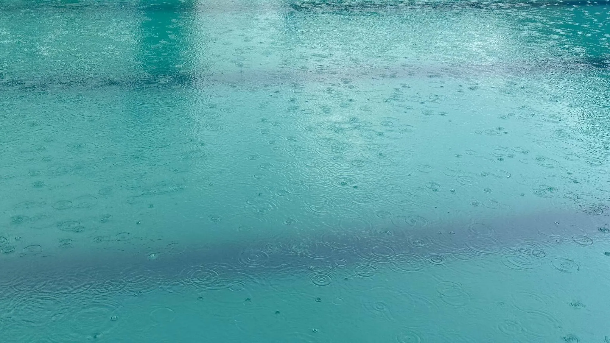 Rain dimpling the surface of clear turquoise pool water