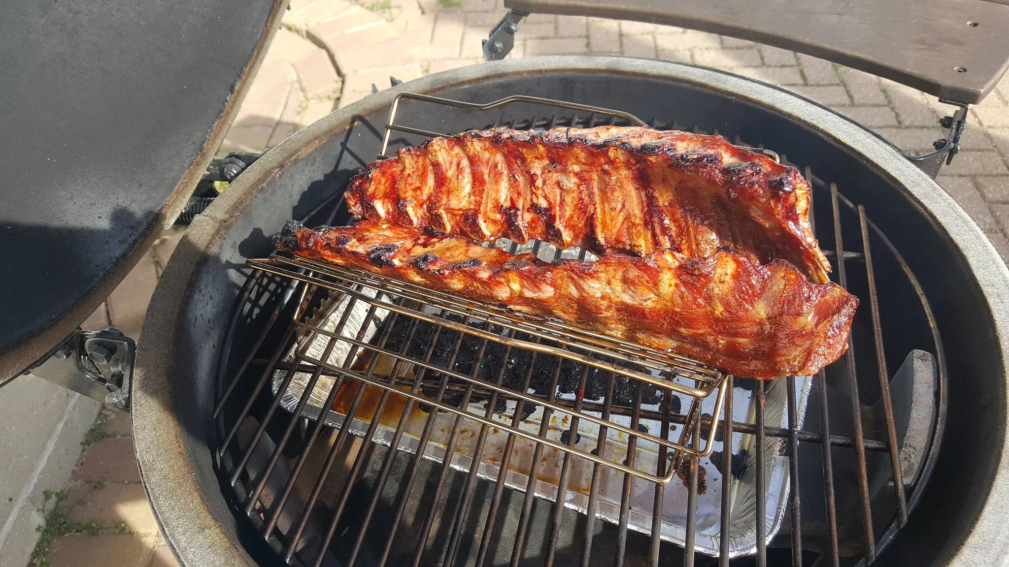 Two racks of glazed ribs on a raised rack inside an open ceramic kamado over a drip pan