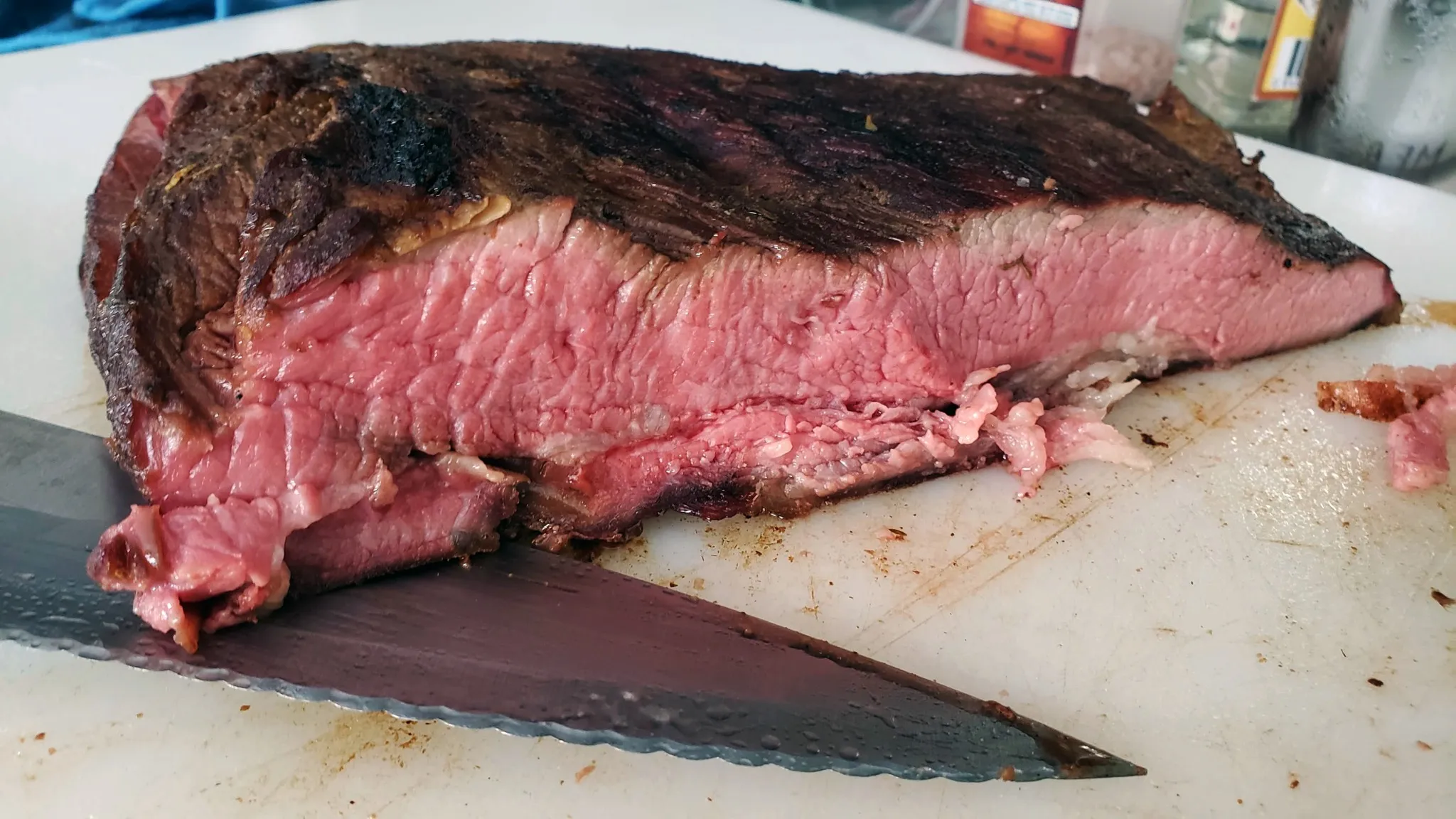 A smoked beef brisket cut open on a white cutting board with a serrated knife in the foreground