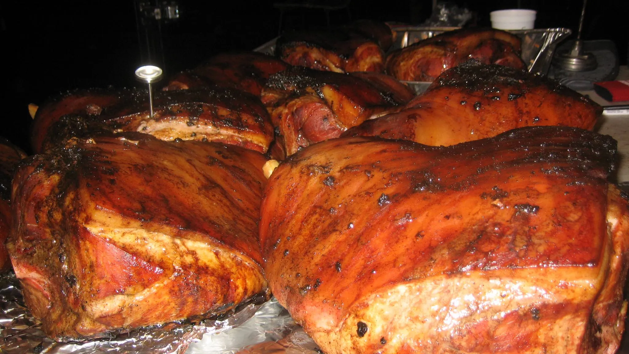 Smoked pork shoulders with a dark bark resting on foil, a probe thermometer standing in one of them