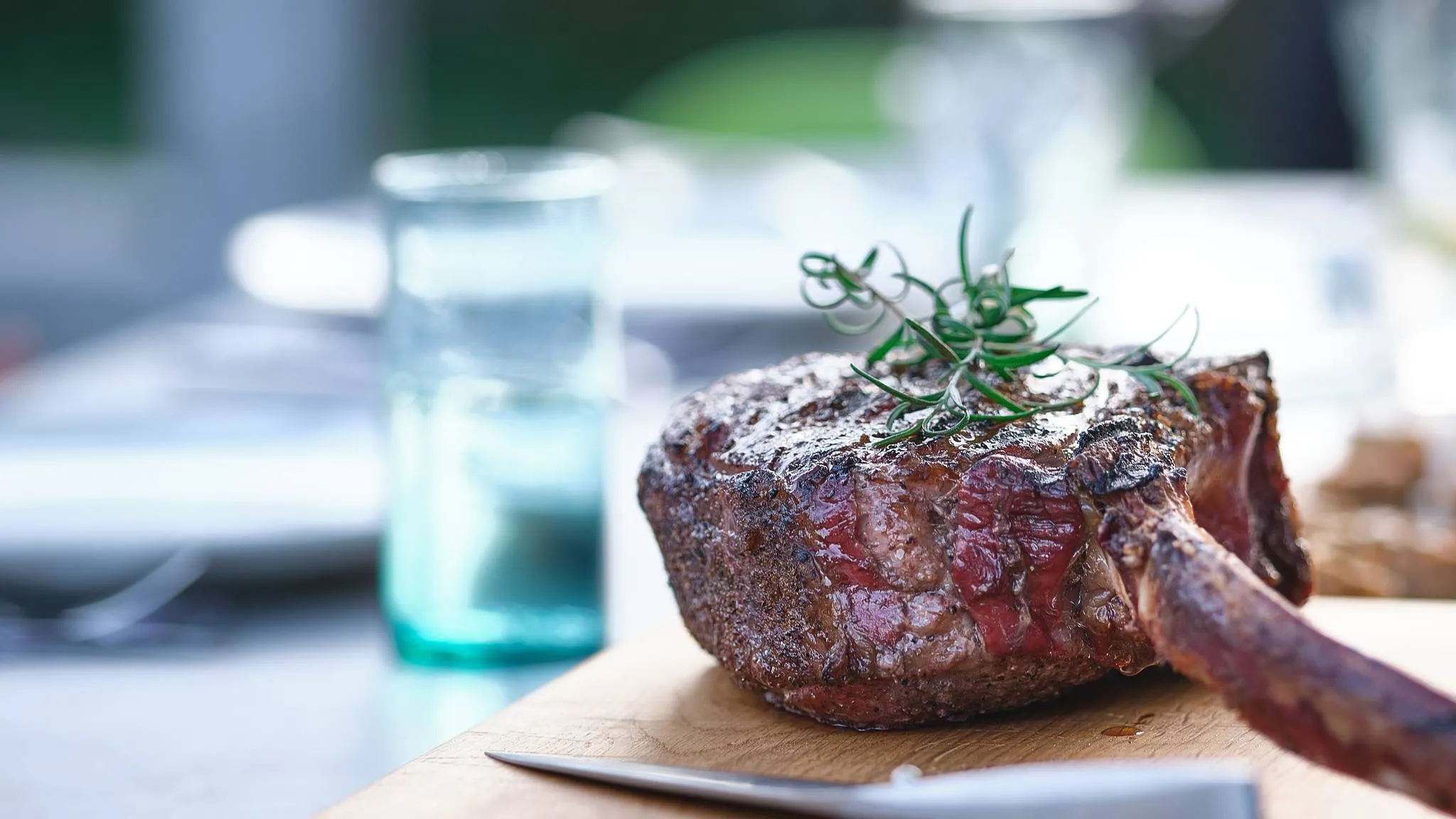 A smoked tomahawk steak with a dark crust and a sprig of rosemary on a wooden cutting board