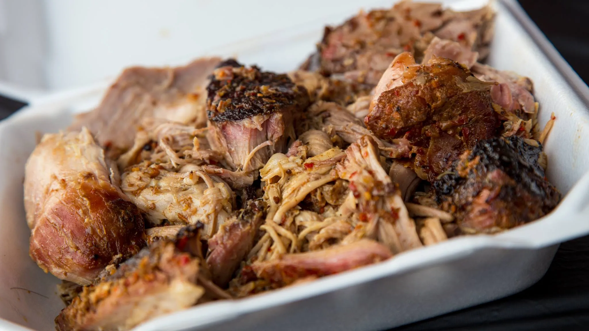 A takeout tray of smoked whole-hog pulled pork with dark bark, entered at a barbecue cook-off